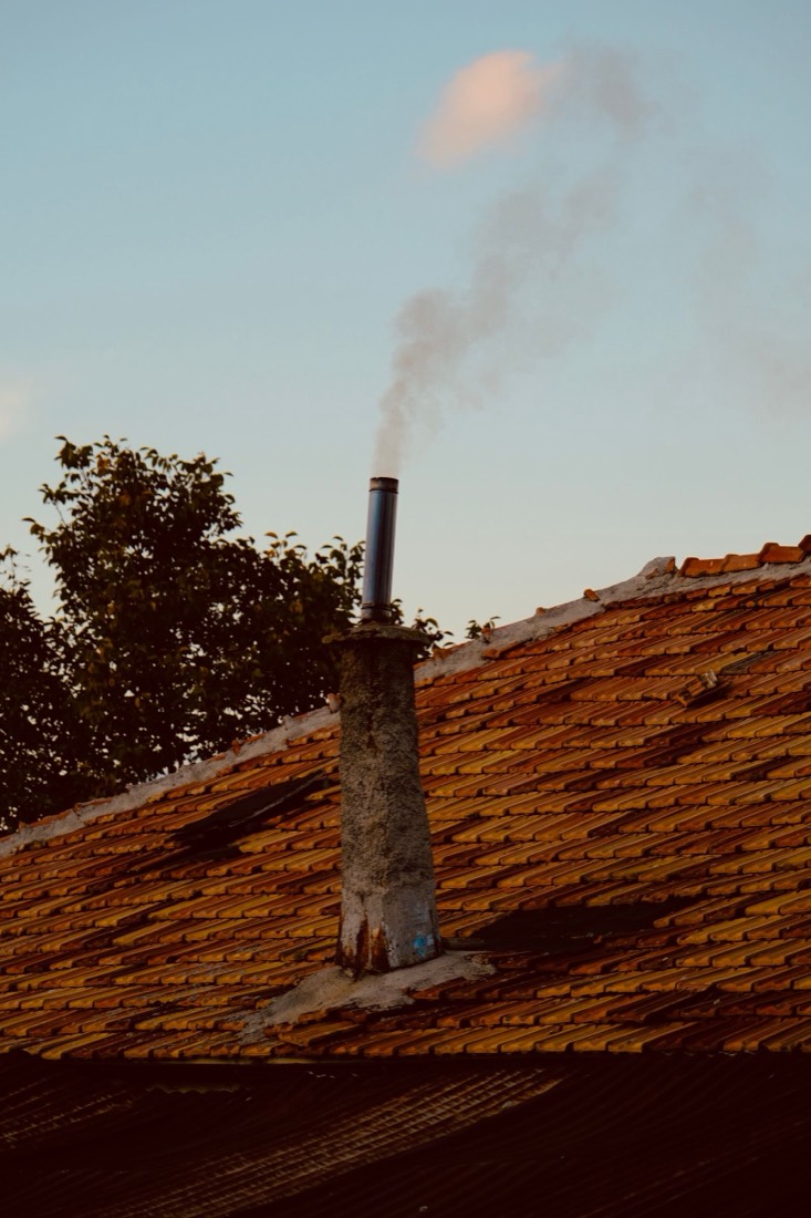 Conduit métallique fumant sur un toit de tuiles au coucher du soleil